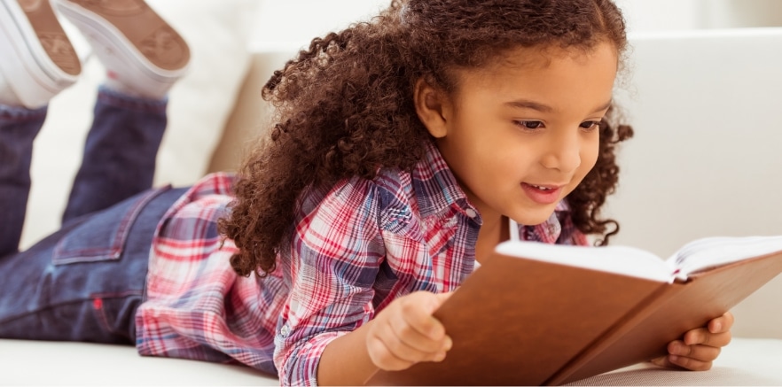 A young girl reading a book on a sofa